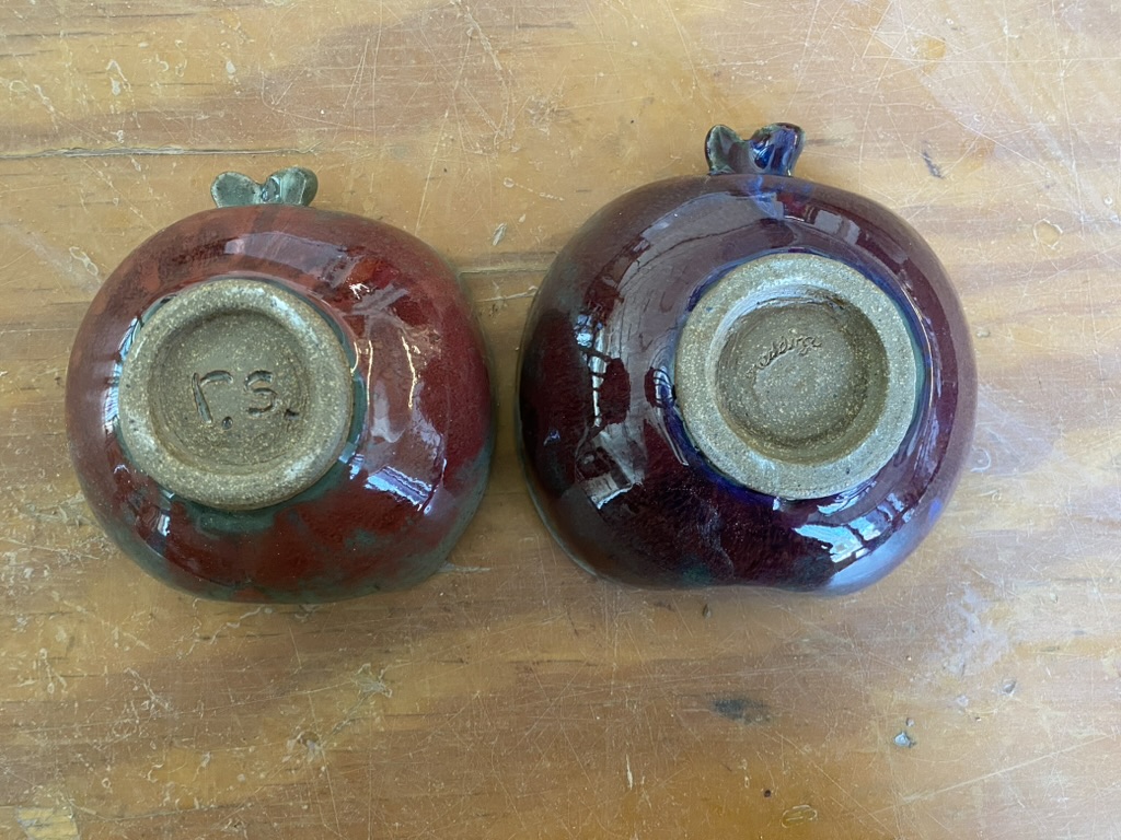 Bottoms of two apple-shaped stoneware bowls with a drippy red-green glaze. One has initials 