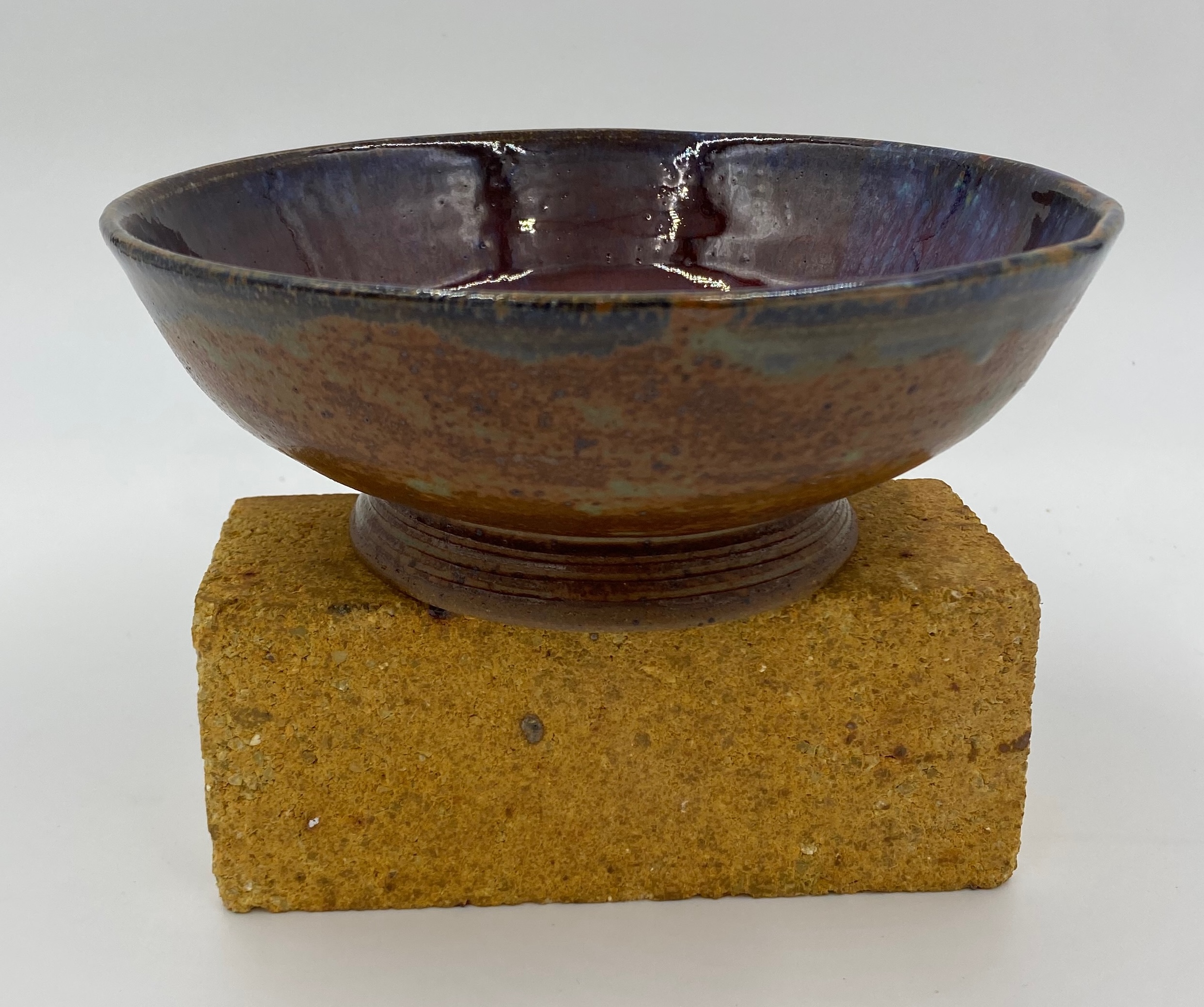 A large shallow bowl with an angled foot. The outside is glazed red-green and the inside is glazed a marbled purple-red.
